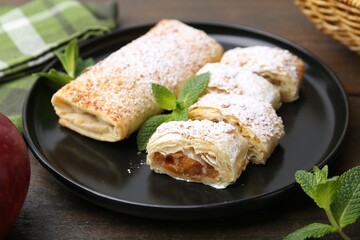 Tasty apple strudels with powdered sugar and mint on wooden table, closeup