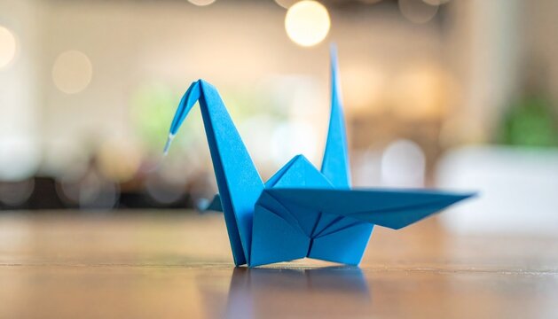 Close up photo of an blue origami bird on a wooden table with a blurry background