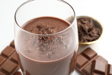 Tasty chocolate milk with shavings and pieces on white table, closeup