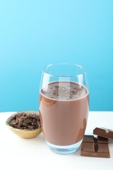Tasty chocolate milk with shavings and pieces on white table against light blue background. Space for text
