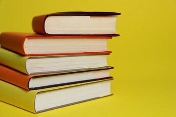 Stack of colorful books on yellow background, closeup. Space for text