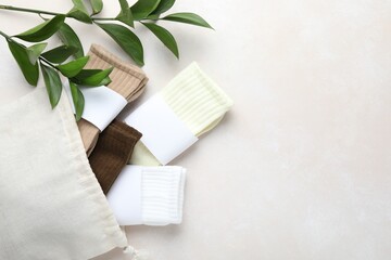 Different soft socks, bag and leaves on light beige background, flat lay. Space for text
