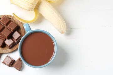 Tasty chocolate milk in cup, pieces and banana on white wooden table, flat lay. Space for text