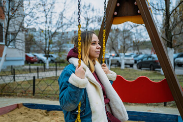 Obraz premium A woman enjoys swinging at a playground surrounded by trees and apartment buildings on a cool autumn day