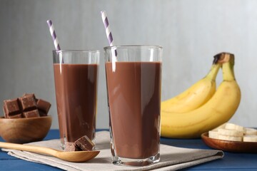 Tasty chocolate milk in glasses, pieces and bananas on blue wooden table, closeup