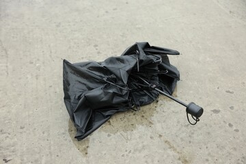 Broken black umbrella on wet asphalt outdoors