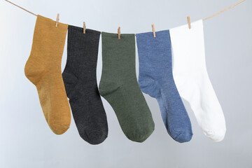 Different socks hanging on washing line against light grey background