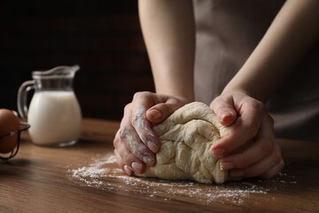 Woman kneading raw dough at wooden table, closeup