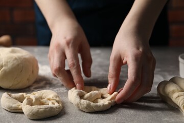 Woman making pretzel at light grey table, closeup