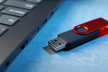 Usb flash drive and laptop on blue textured table, closeup
