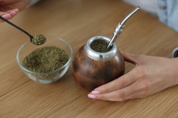 Woman making traditional yerba mate tea at wooden table indoors, closeup