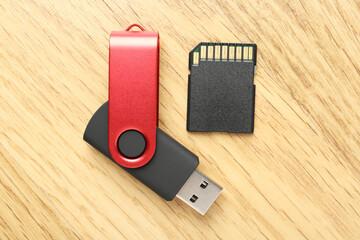 Flash drive and SD memory card on wooden background, flat lay
