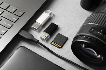 Flash drives, SD memory card, external hard disk, laptop and camera on gray textured table, closeup