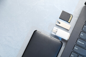 Flash drives, SD memory card, external hard disk and laptop on gray textured table, flat lay. Space...