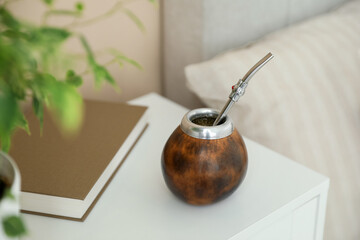 Traditional yerba mate tea and book on bedside table indoors