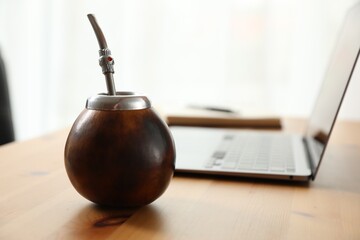 Traditional yerba mate tea and laptop on wooden table, closeup