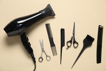 Combs, dryer and other hairdresser's tools on beige background, flat lay