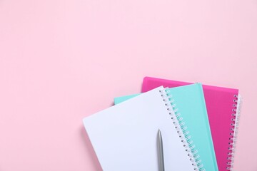 Pen and notebooks on pink background, top view. Space for text