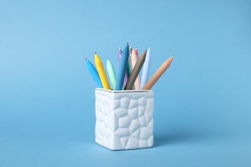 Ballpoint pens in holder on light blue background, closeup