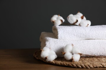 Stack of clean towels and cotton flowers on wooden table against dark grey background, closeup....