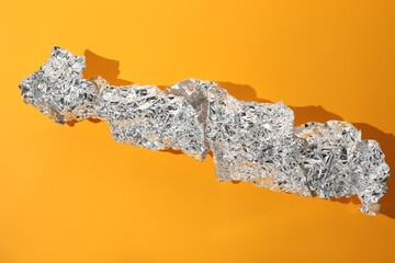 Crumpled piece of aluminum foil on orange background, top view