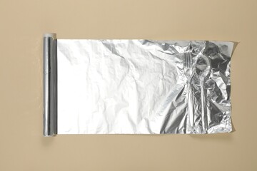 Roll of aluminum foil on beige background, top view