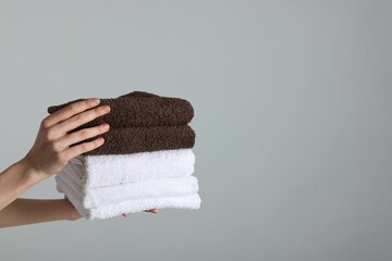 Woman holding stack of clean towels on light background, closeup. Space for text