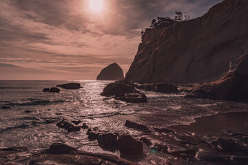 Fototapeta premium Pacific Northwest cliffside beach in late afternoon sunlight with clouds. Oregon beach with rolling waves and sand. Ocean landscape, background, wallpaper