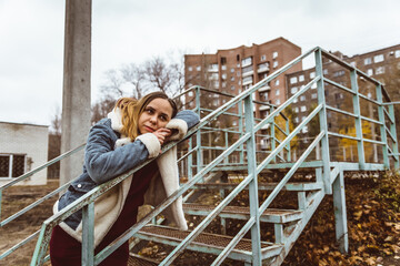 Young woman leans against green metal railing while pondering in an urban setting during a cloudy...
