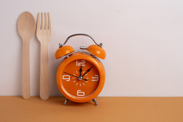 Alarm clock, fork and spoon on white plate. Time to eat concept. Diet