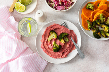 A healthy breakfast with beet hummus, baked sweet potato, and broccoli, topped with a fresh radish and cabbage salad, offering protein and nutrients