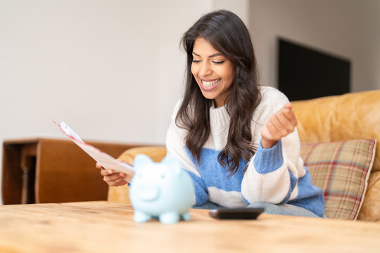 Woman expresses joy while reviewing financial documents at home with a piggy bank on the table