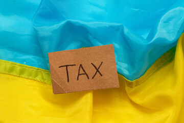 The inscription tax on a piece of cardboard against the background of the blue and yellow flag of...