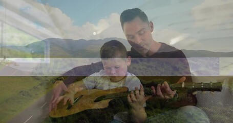 Father guiding son playing guitar in living room, using animated chord charts for music education