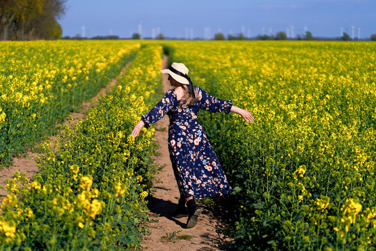 Woman in floral dress walking and spinning joyfully in blooming rapeseed field on a sunny spring day. A peaceful rural landscape capturing the essence of freedom and connection with nature.