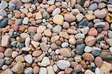 Colorful collection of smooth beach pebbles and natural stones. Top view of a diverse assortment of rounded rocks with various textures and colors on coastal sand.