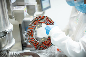 A female worker in sterile gloves holds a circular mold containing capsules in the production of...