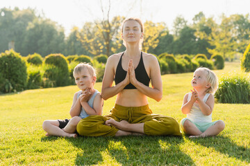 Mother with children doing yoga exercise on nature. Healthy lifestyle of family.