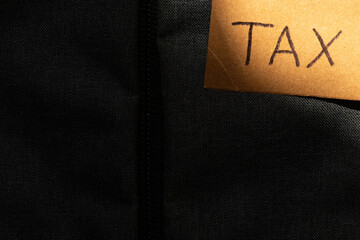 A paper card with the inscription tax illuminated by a beam of light on a dark background of fabric
