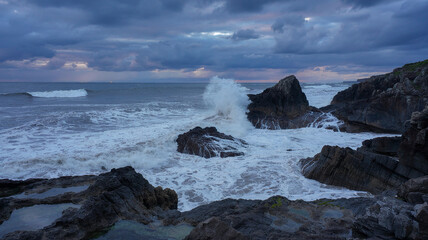 Obraz premium Waves crash on rocks under a cloudy sky