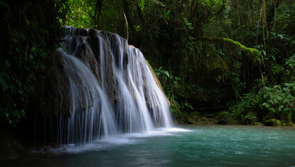 Serene long exposure wide shot of a multi-tiered waterfall cascading into a turquoise pool surrounded by lush green tropical rainforest jungle foliage