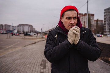Man in red beanie and gloves standing outdoors in cold weather near urban area