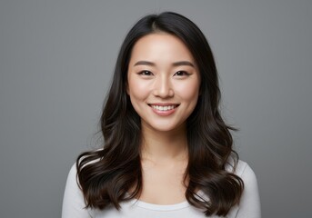Obraz premium Portrait of smiling asian woman with long dark hair against a gray background