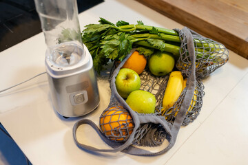 Mesh produce bag sitting beside personal blender on white countertop, holding apples, bananas
