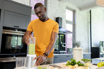 African American man blending smoothie on counter in kitchen, with compost bin, copy space
