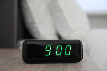 Digital alarm clock showing 9:00 o'clock on bedside table indoors