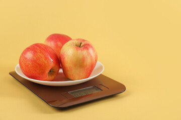 Electronic kitchen scale with apples on yellow background, closeup. Space for text