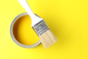 Can of bright paint and brush on yellow background, top view. Space for text