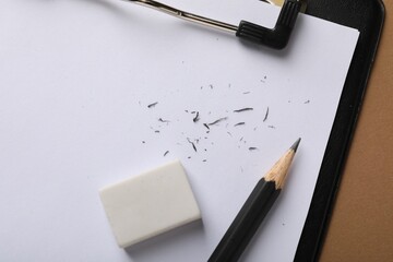 Eraser, pencil, scraps and clipboard on brown background, top view