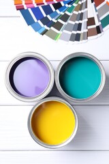 Cans of bright paints and color palettes on white wooden table, flat lay